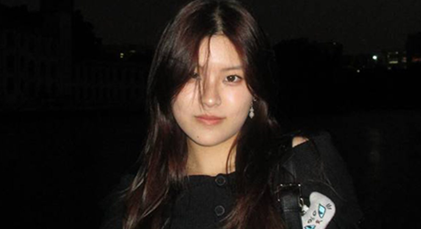 Headshot of a young woman with dark hair over her face, in the dark.