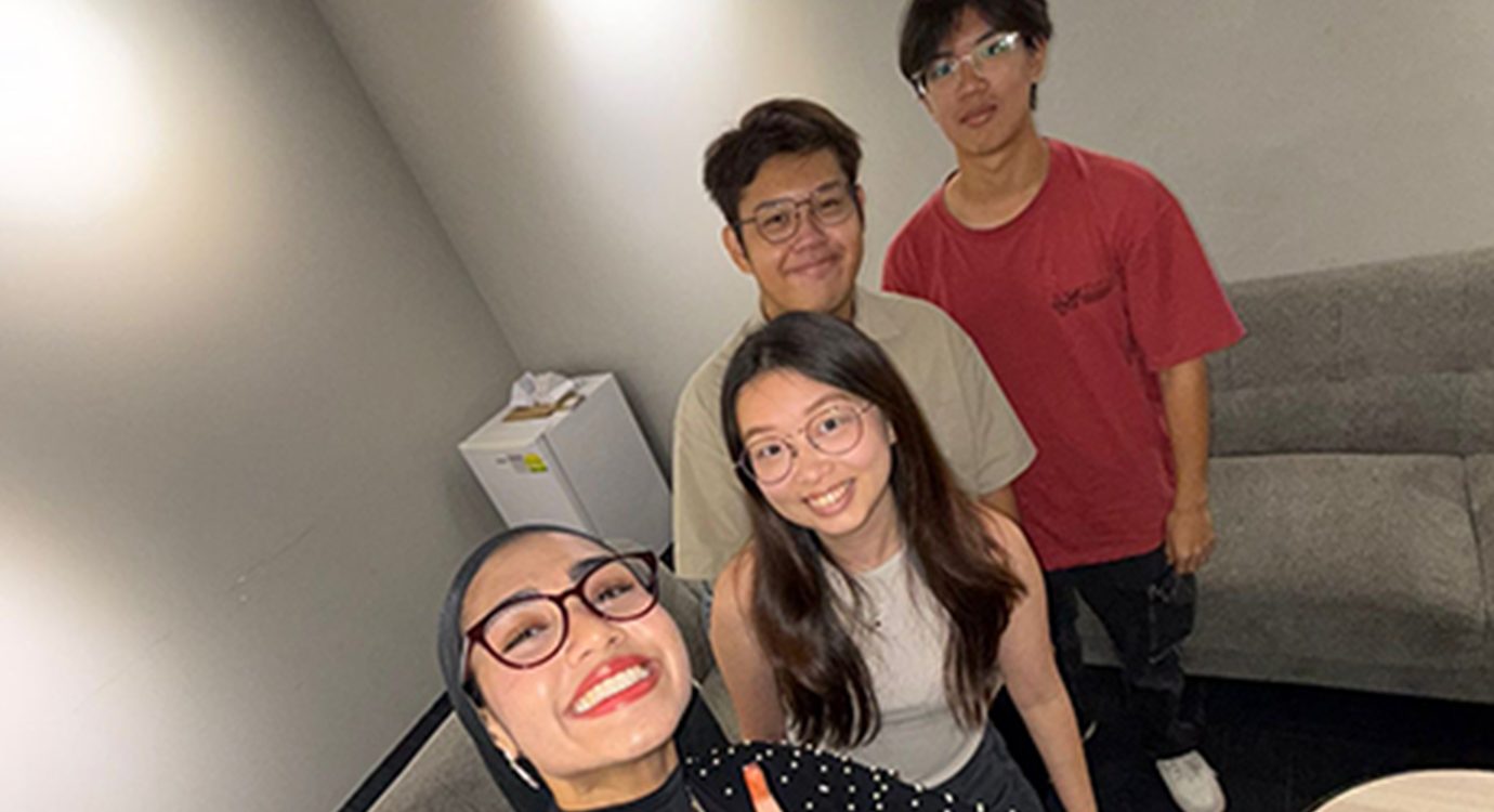 Group photo of four smiling young adults indoors.