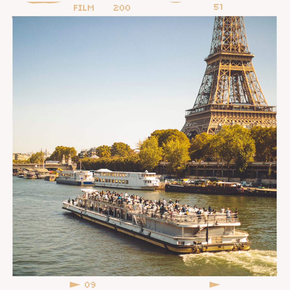 A scenic view of the Eiffel Tower and a crowded tour boat cruising on the Seine River in Paris.