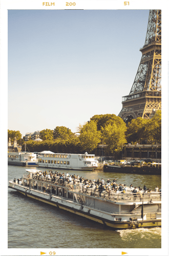 Eiffel Tower and a crowded tour boat on the Seine in Paris under a clear sky.