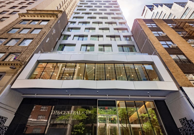 Modern "THE CENTRAL AT 5TH HILTON CLUB" building flanked by older buildings.