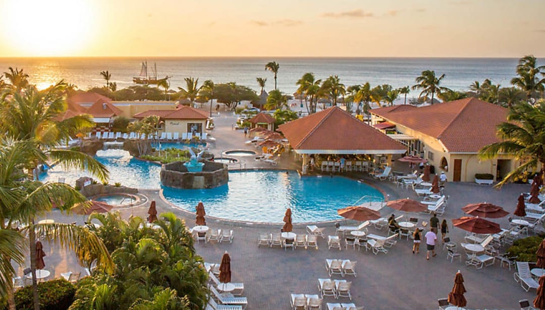 Tropical resort at sunset with multiple pools, palm trees, and ocean views.