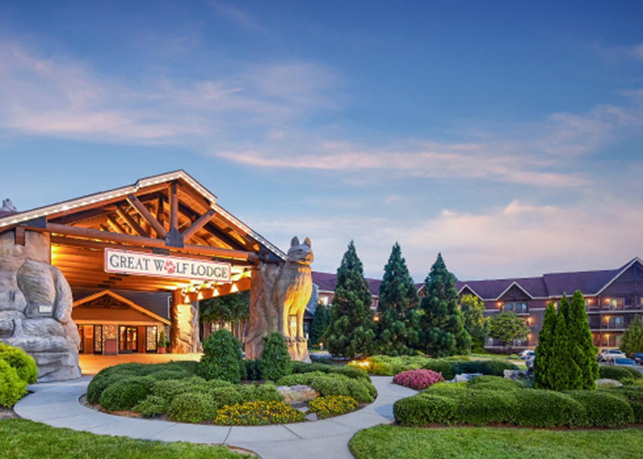 Great Wolf Lodge entrance with wolf sculptures, a sign, and landscaping at dusk.