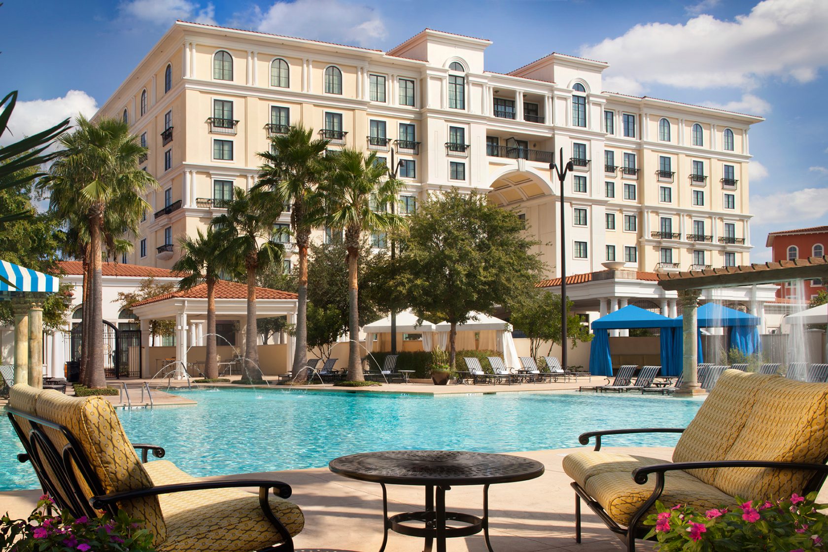 Luxury hotel with a large swimming pool, palm trees, and lounge chairs.