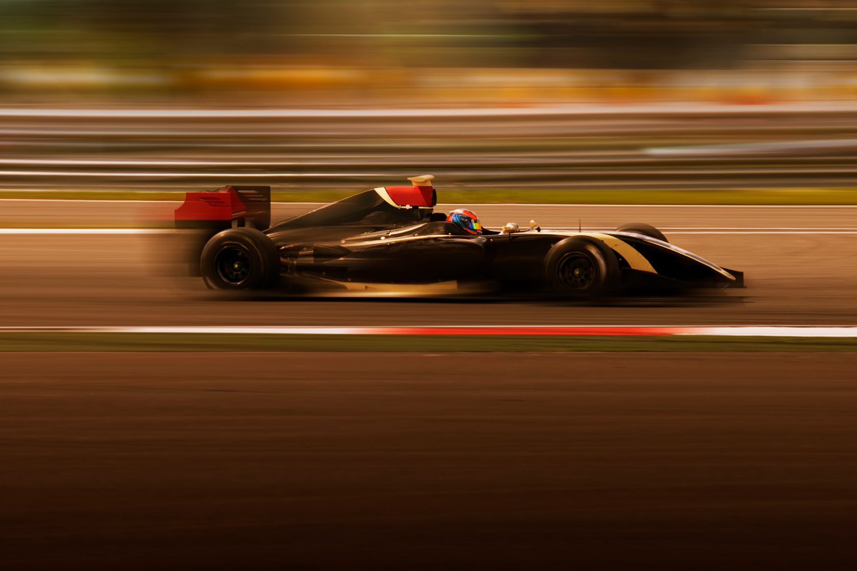 A high-speed, motion-blurred shot of a black and red formula racing car on a track.