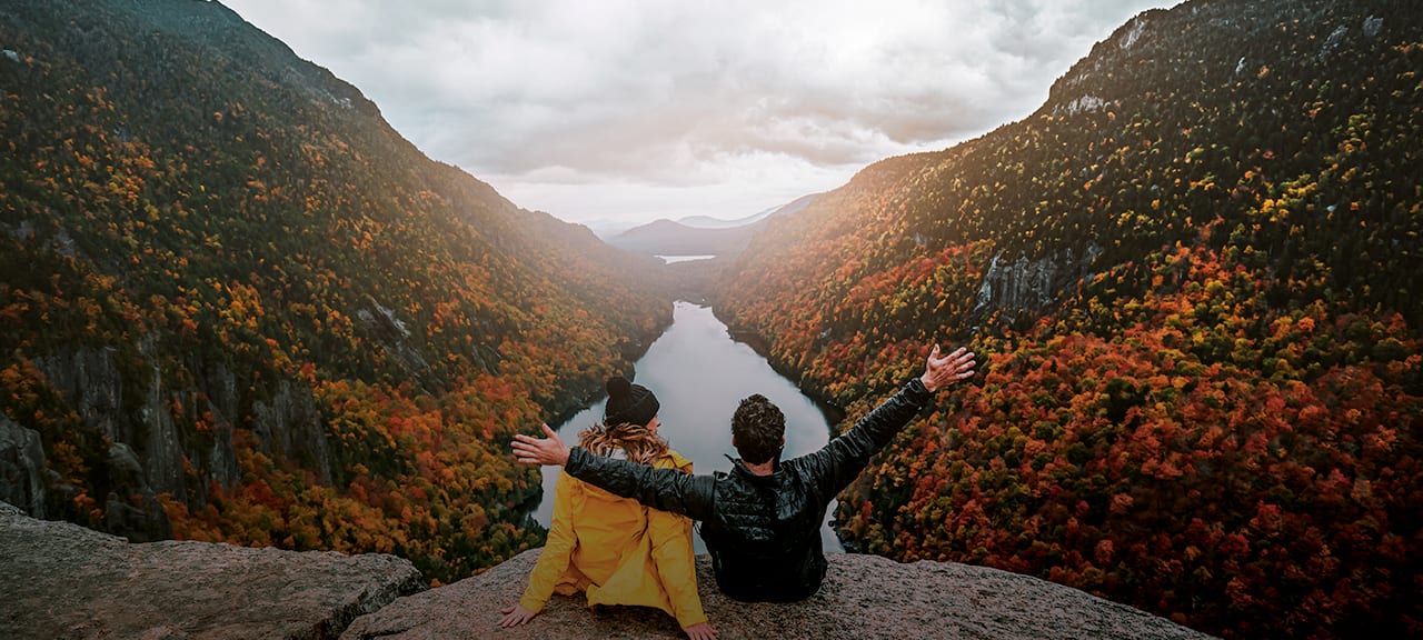 Two people on cliff overlooking colorful autumn valley.