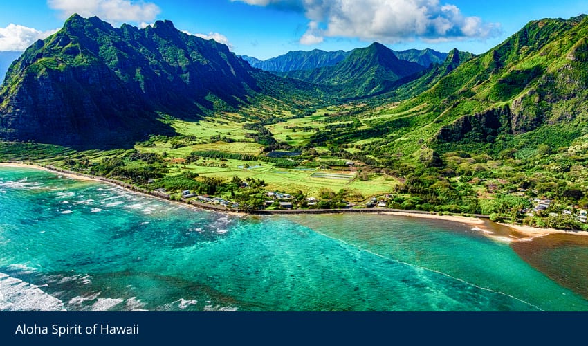 Aerial view of a Hawaiian coastal valley with lush green mountains and turquoise ocean.