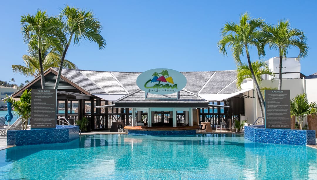 Swimming pool in front of Cabana Beach Bar & Restaurant with palm trees under a blue sky.