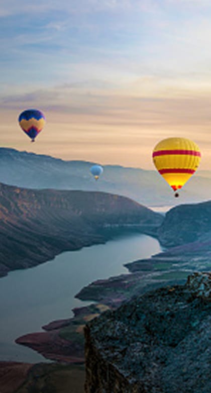 Colorful hot air balloons over river in mountain canyon.