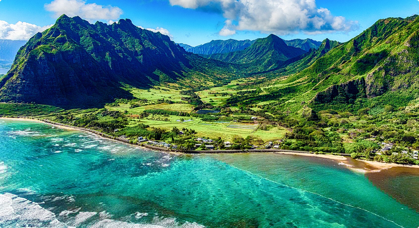 Lush green mountains, valley, coastal road, and vibrant turquoise ocean.