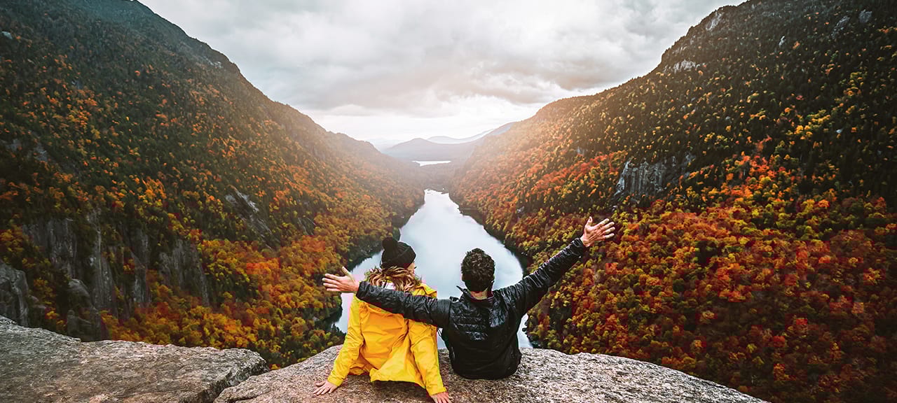 Couple overlooks colorful autumn river valley from peak.