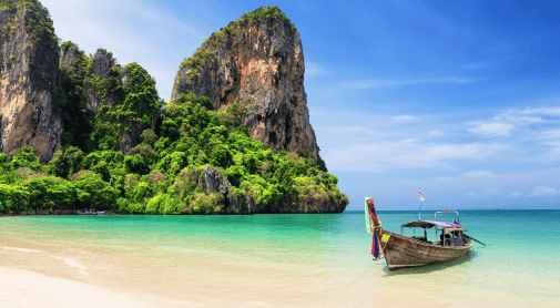 A longtail boat rests on a sandy beach with clear turquoise water and towering limestone cliffs.