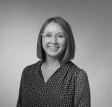 Grayscale headshot of a smiling woman with short hair and glasses, wearing a patterned shirt.