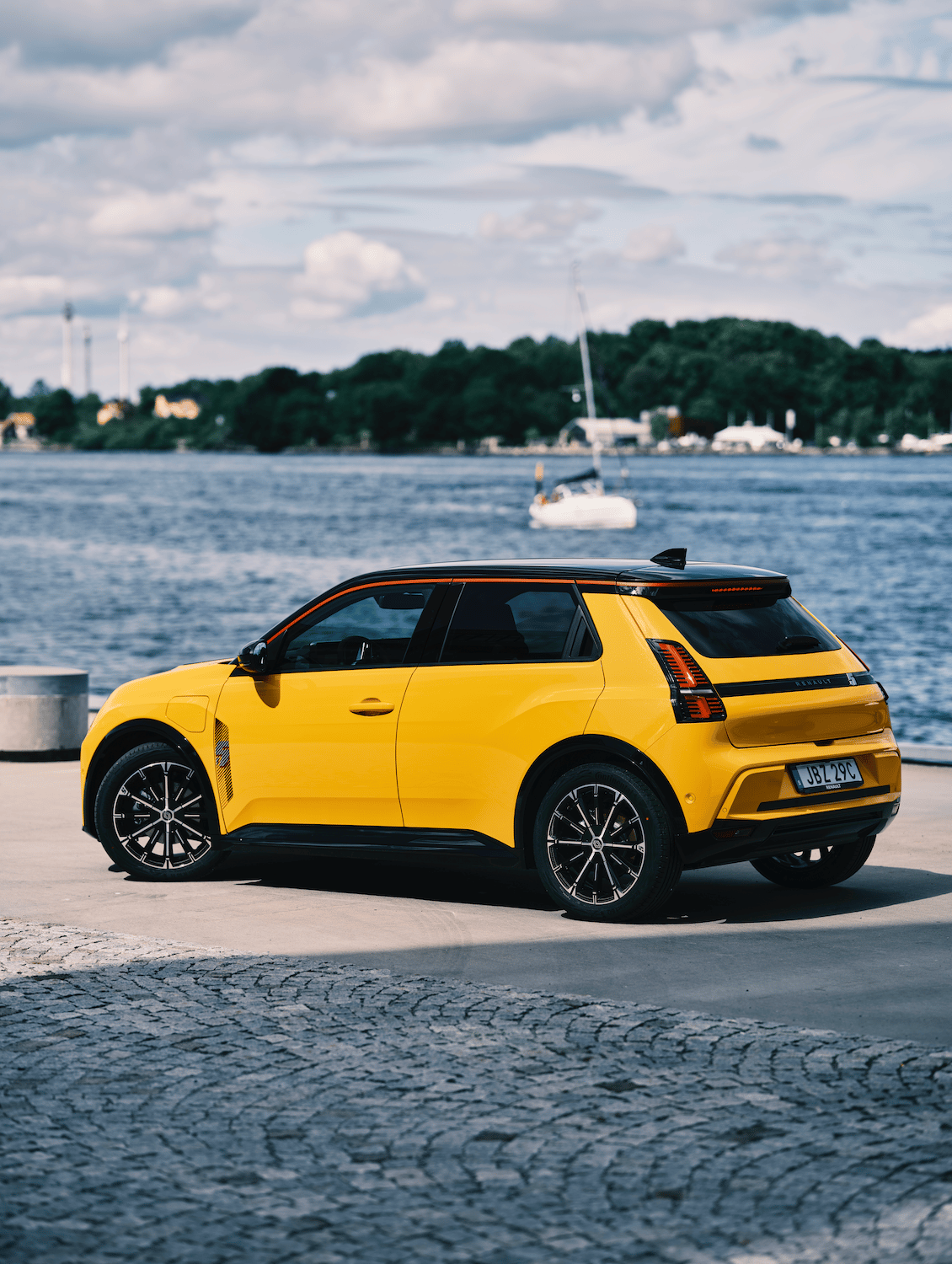 A vibrant yellow Renault 5 E-Tech electric car parked by a scenic waterfront on a sunny day.