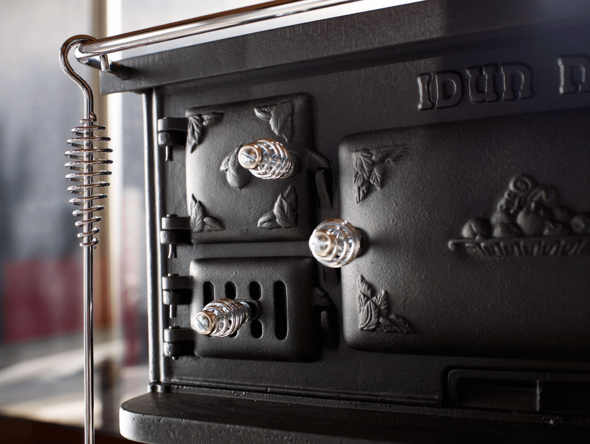 Close-up of a decorative black cast iron stove with chrome spring handles and a matching tool.