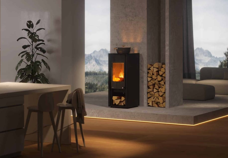 Modern room with a wood-burning stove, stacked firewood, large plant, kitchen island, and mountain view.