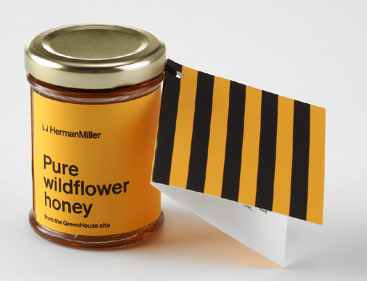 A jar of HermanMiller pure wildflower honey with orange label and striped tag.