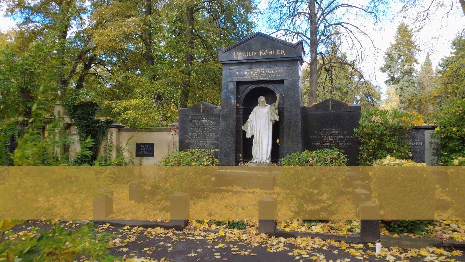 Cemetery monument with a Jesus statue, gravestones, and autumn leaves.