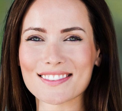 A close-up of a smiling woman's face with long brown hair and blue eyes.
