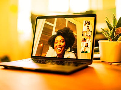 Smiling Black woman on laptop video call with others, a plant on the desk.