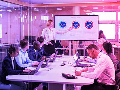 A businesswoman presents market share data on a screen to colleagues in a modern meeting room.