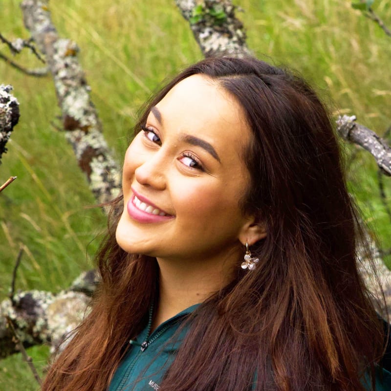 Smiling woman with long dark hair and flower earrings outdoors.