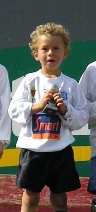 A young boy with curly blonde hair, wearing a white shirt, holding a trophy that says "Smart Club."