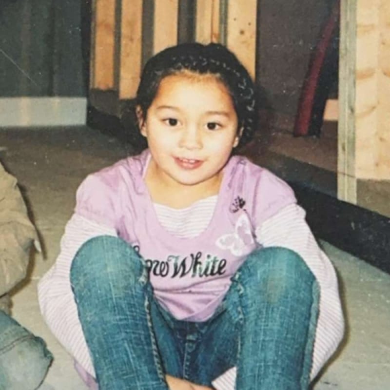Young girl with braided hair smiles, sitting on floor in 'Snow White' shirt and jeans.