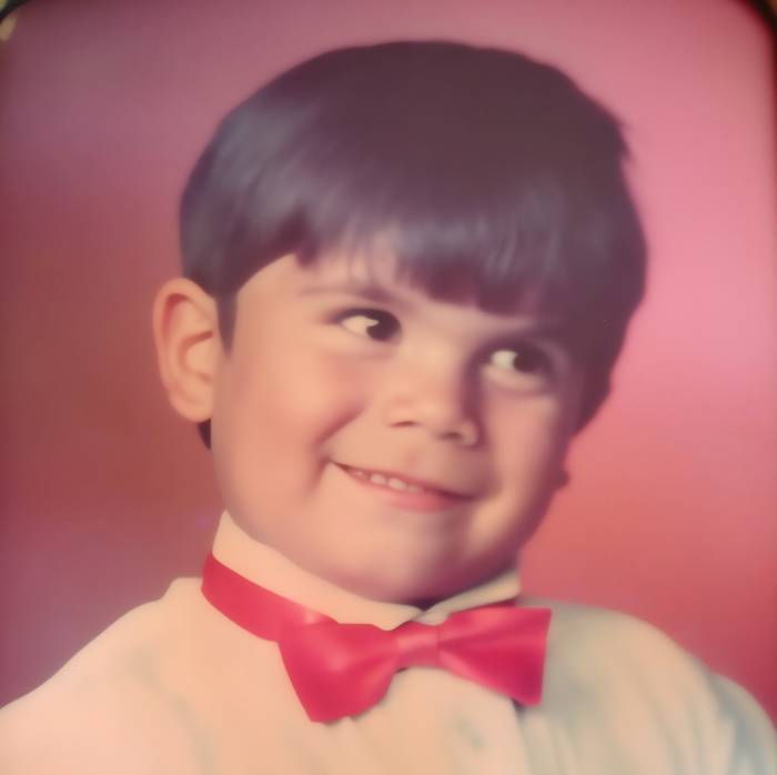 Smiling young boy with dark hair and a red bow tie, looking sideways.