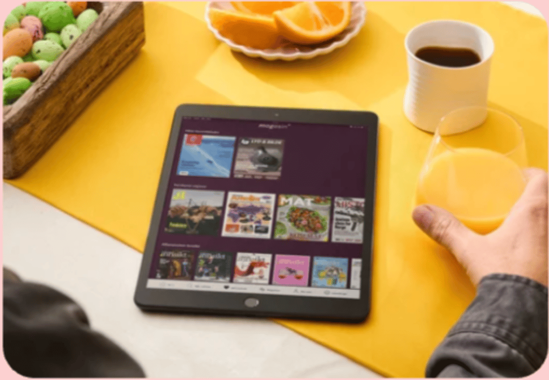 Person reading digital magazines on a tablet with breakfast items.