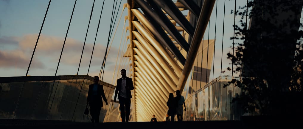 Silhouetted people on a modern architectural bridge at sunset.