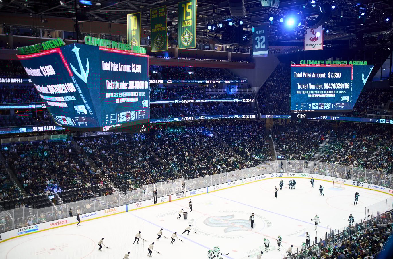 Interior of Climate Pledge Arena with hockey players on ice, spectators, and screens displaying a $7,650 raffle.