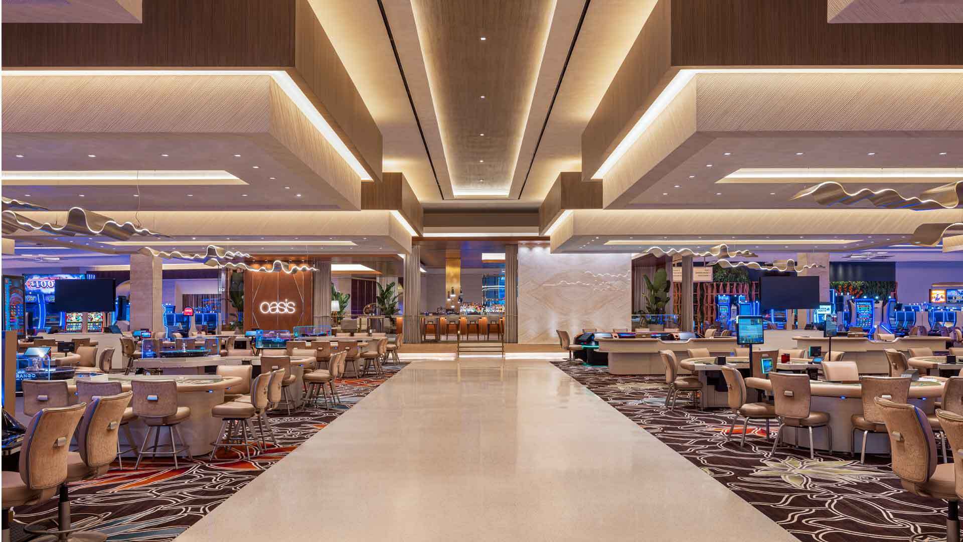 Luxurious casino floor with gaming tables, slot machines, a bar, and a modern, illuminated ceiling.