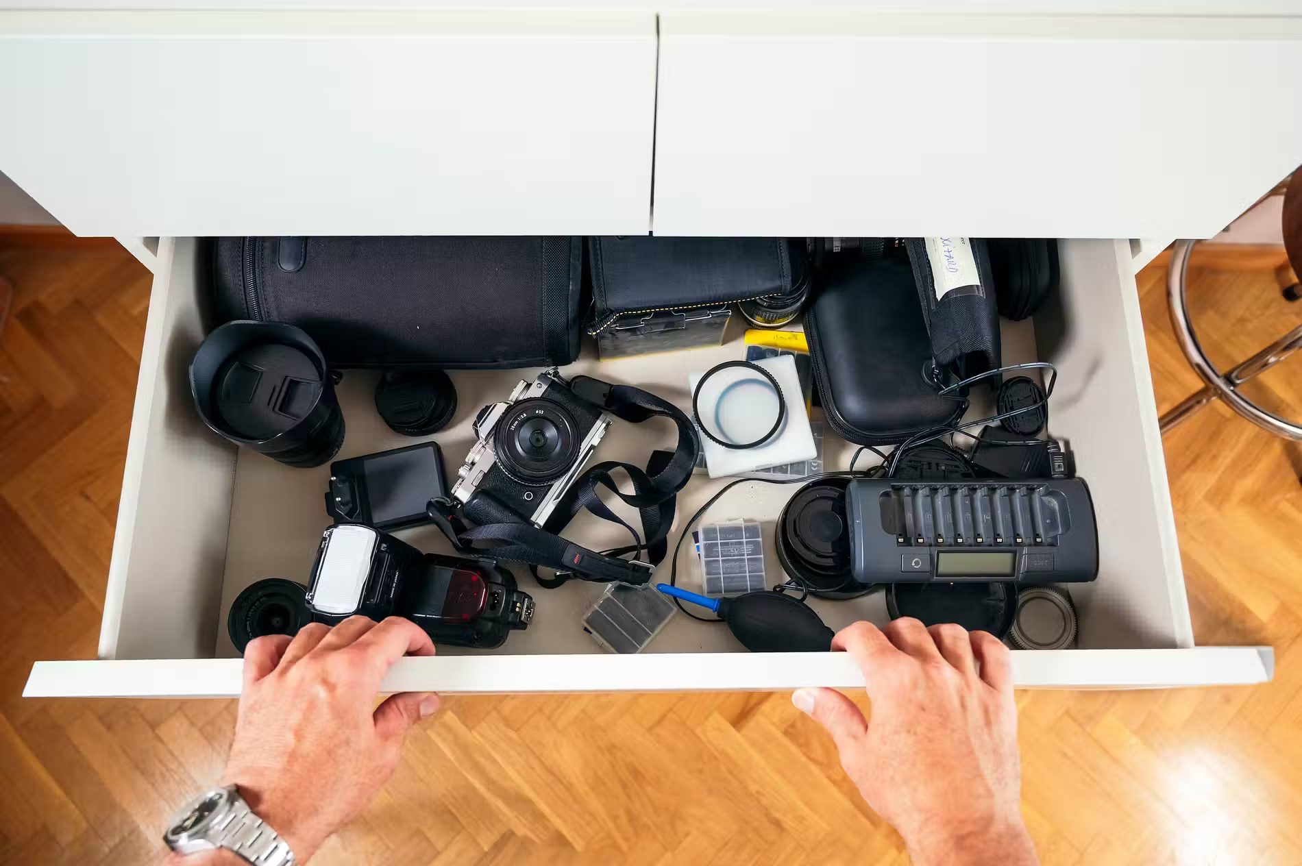 A drawer filled with various photography equipment, including a camera, lenses, flash, battery charger, and accessories.