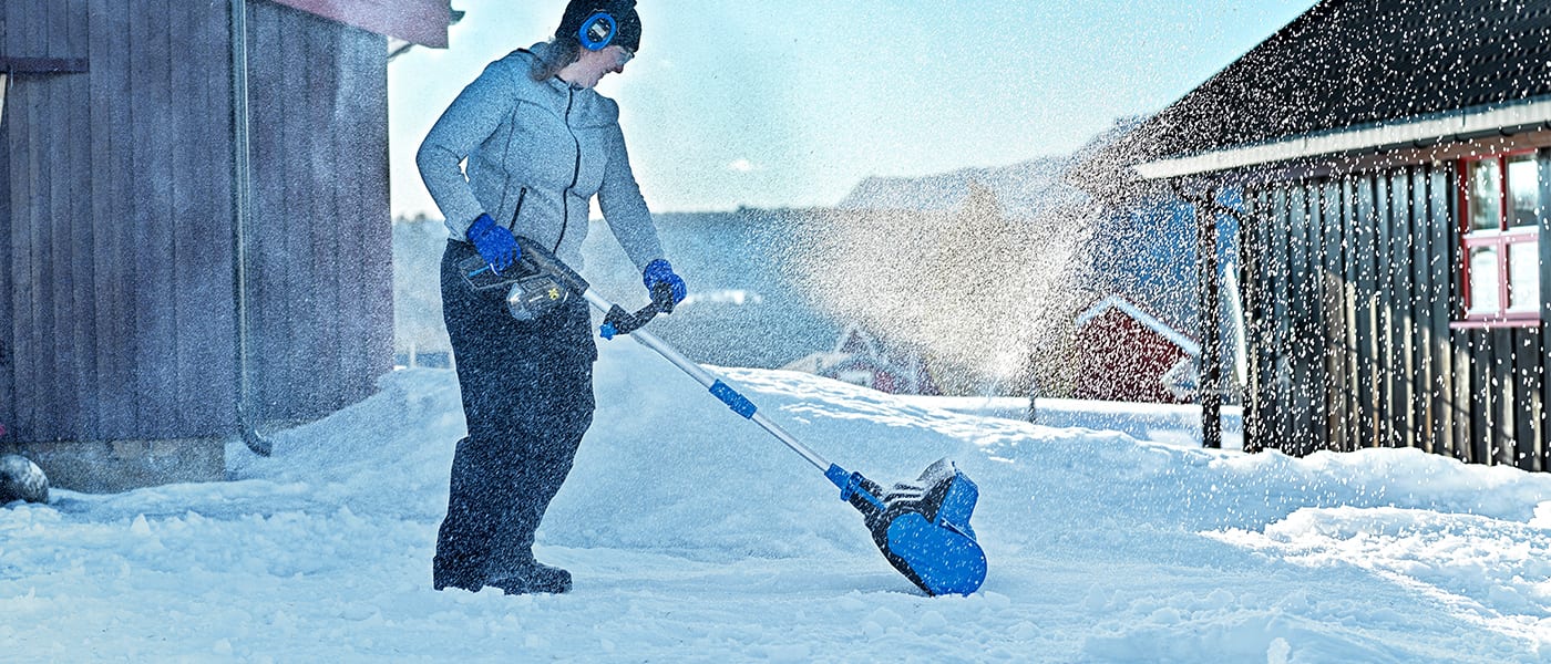 Woman uses blue electric snow shovel, actively clearing snow.