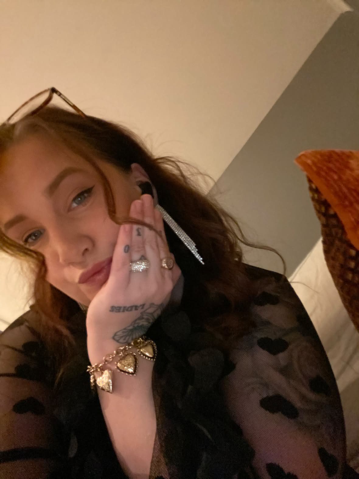 Close-up of a woman in a black heart-patterned top, wearing glasses, rings, and a heart bracelet.