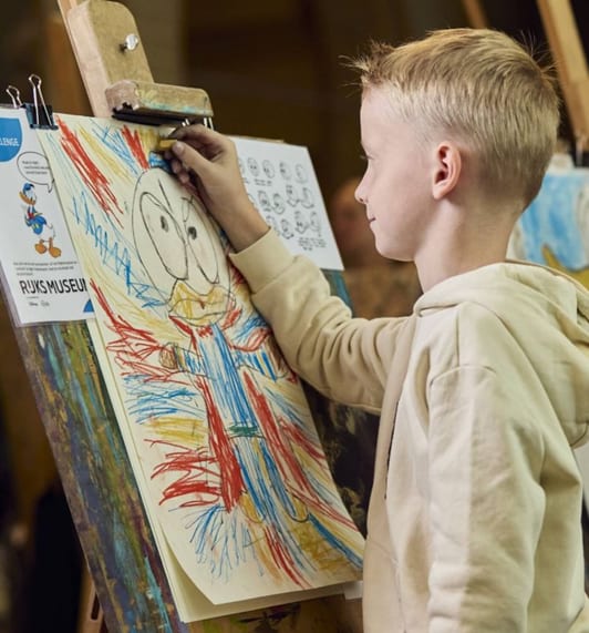 Young boy drawing a colorful cartoon character on an easel with crayons.