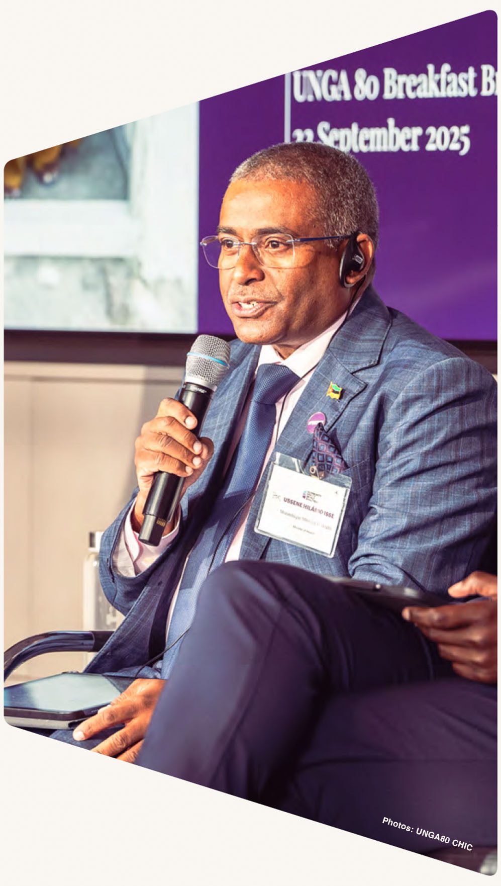 A man in a suit and glasses speaks into a microphone at an event with "UNGA 80" text visible.