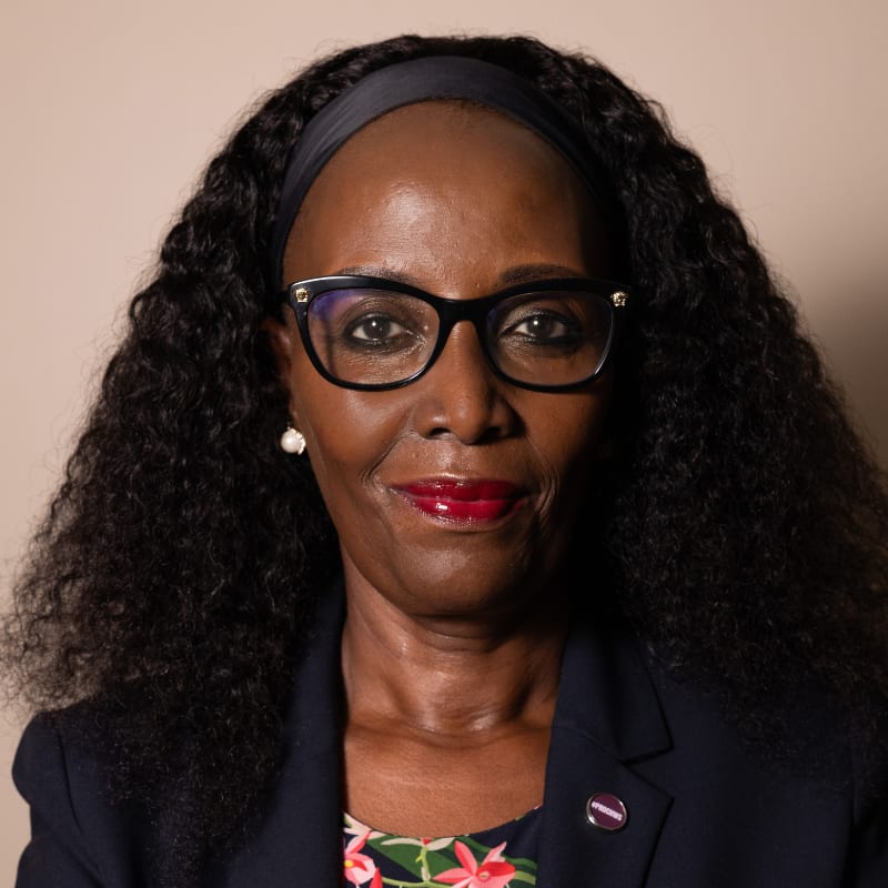 Headshot of a smiling Black woman with glasses, curly hair, and a dark blazer.