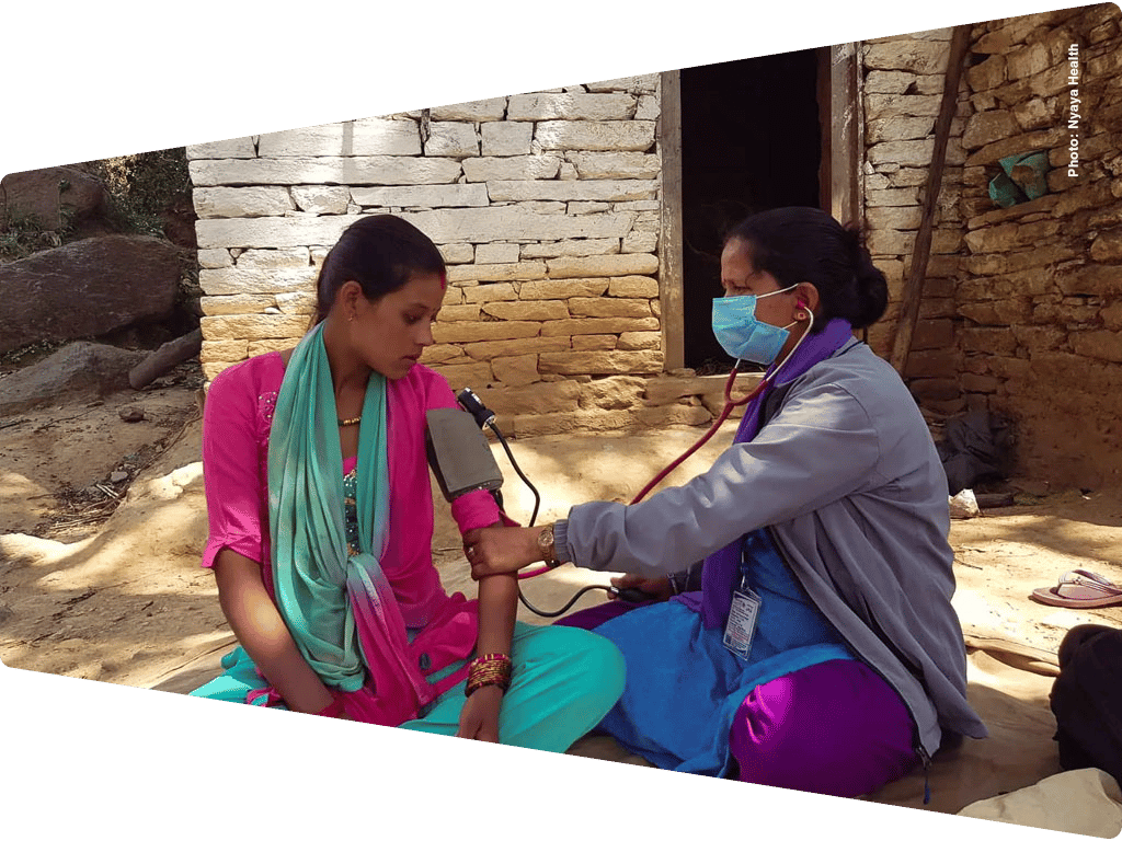 Healthcare worker takes blood pressure of a young woman outdoors in a rural setting.