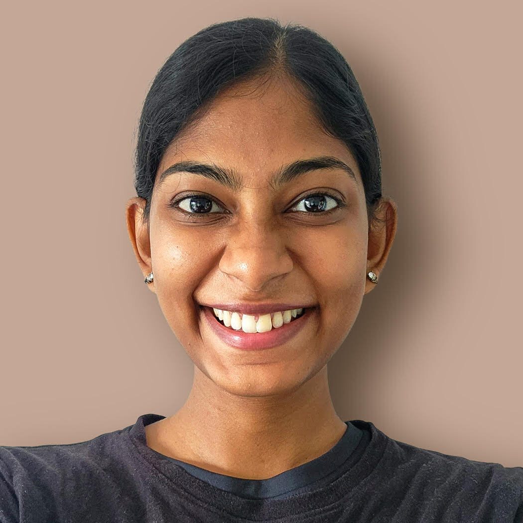 A smiling young woman with dark hair and eyes, wearing a black t-shirt, looking directly at the camera.