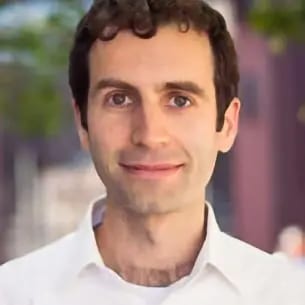 Headshot of a smiling man with dark, curly hair and a white collared shirt looking directly at the camera.