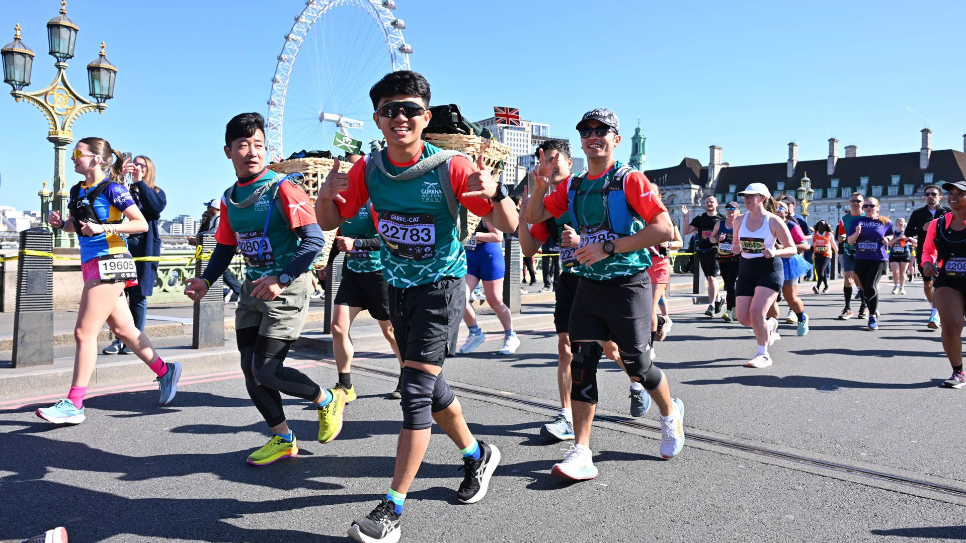 Marathon runners carrying baskets, smiling with London Eye in background.