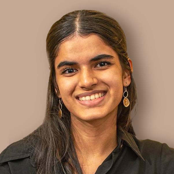 A young woman with long dark hair and gold earrings smiles broadly, looking directly at the viewer.