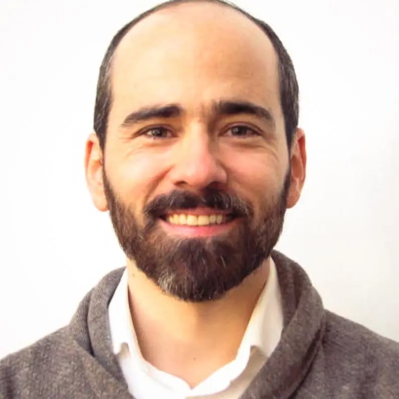 Headshot of a smiling man with a beard and short hair, wearing a white shirt and grey cardigan.