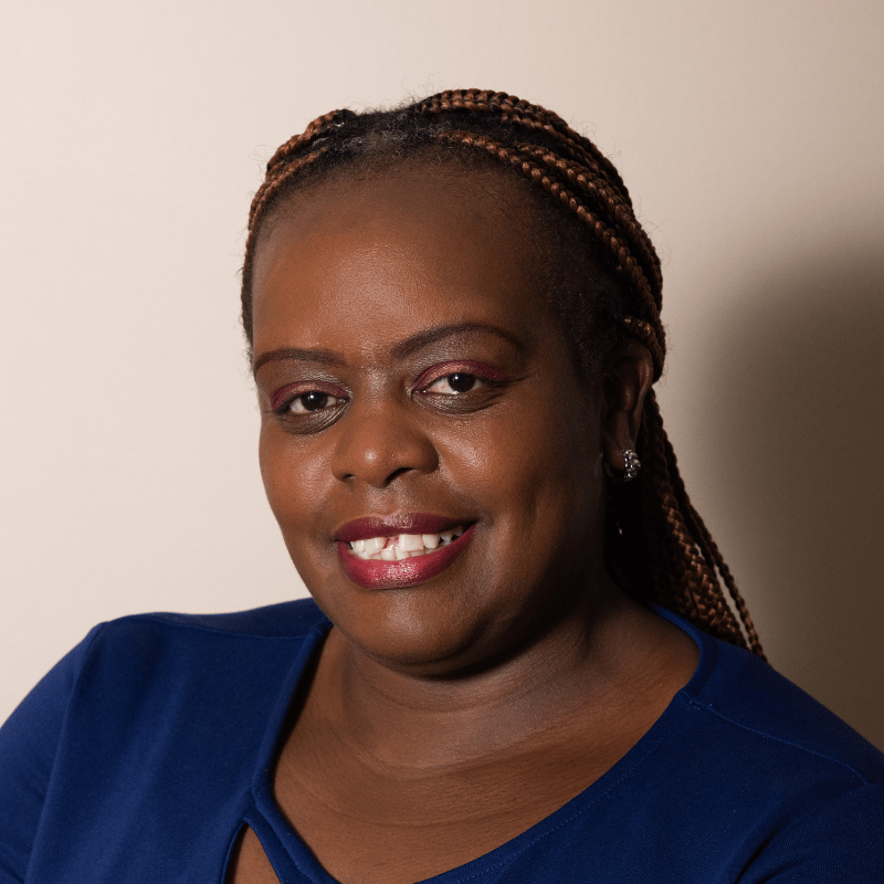 A smiling Black woman with braided hair and a blue top looks directly at the viewer.