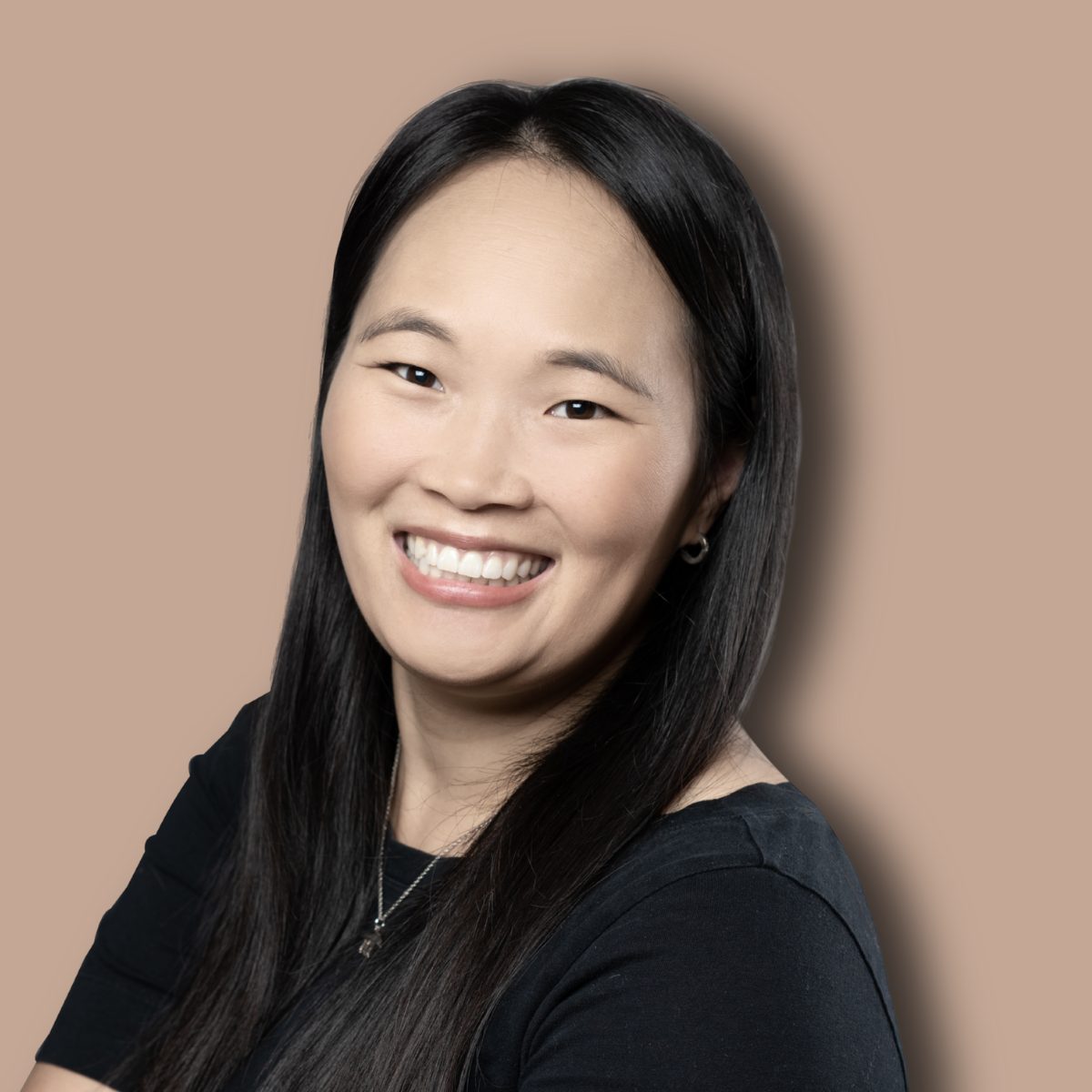 Smiling Asian woman with long dark hair, wearing a black top and silver necklace.