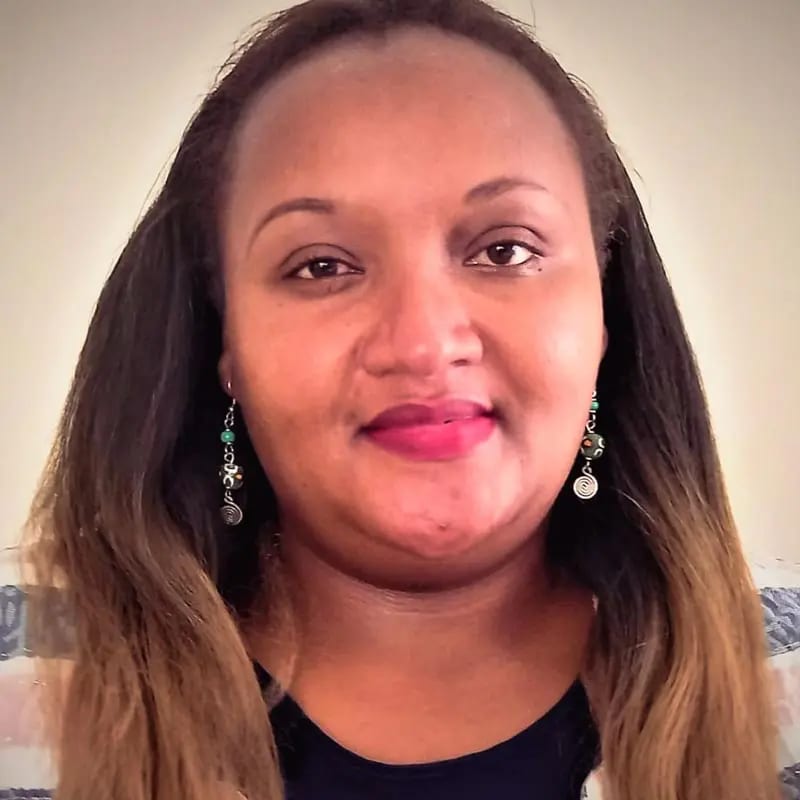 A woman with long dark hair and beaded earrings looks directly at the camera with a slight smile.