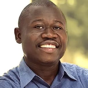 Close-up headshot of a smiling Black man in a blue striped shirt.