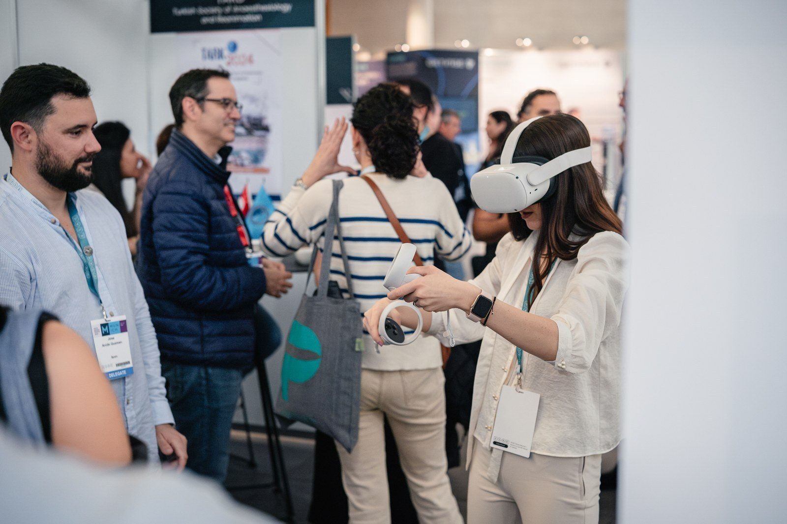 Woman in white VR headset holding controllers at an event, surrounded by people.